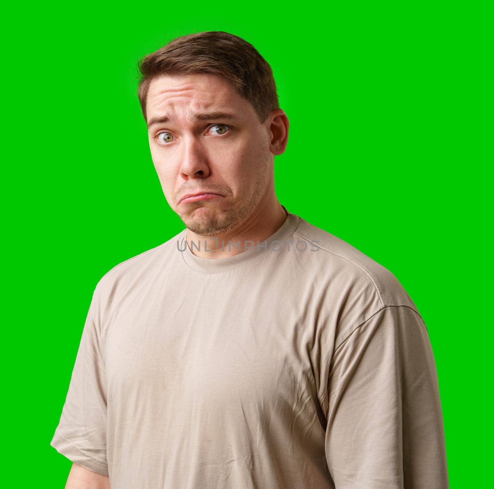 Man with a neutral expression poses against a bright green backdrop in studio
