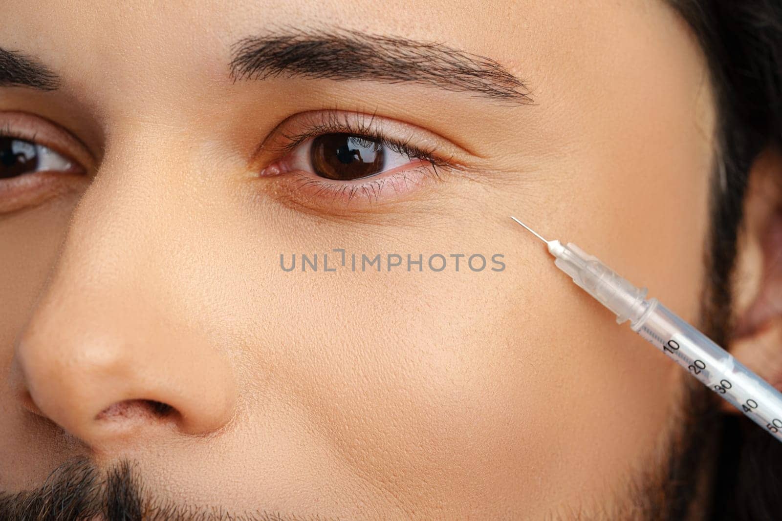 Man receiving facial treatment with a syringe for enhancing appearance, likely in a modern clinic