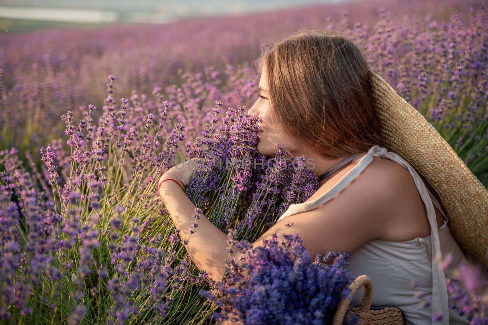 A woman is sitting in a field of lavender flowers. She is wearing a straw hat and holding a basket of flowers. The scene is peaceful and serene, with the woman enjoying the beauty of the flowers