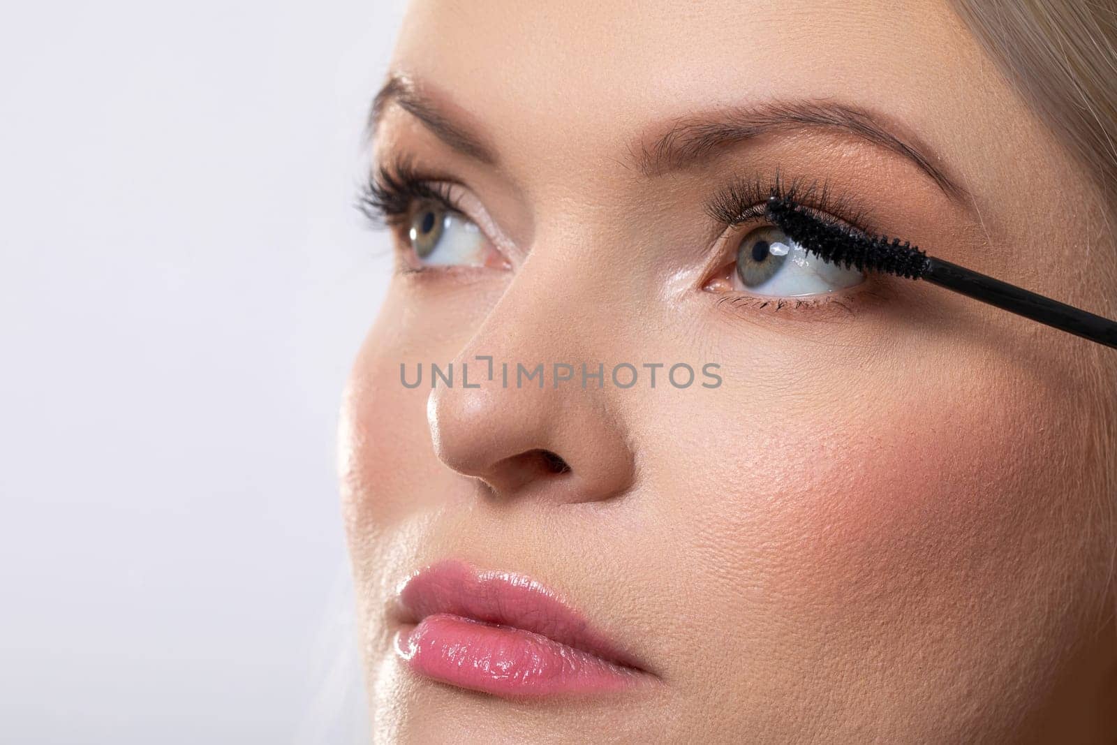 A captivating closeup of a beautiful woman applying her mascara, showcasing her striking features and flawless skin