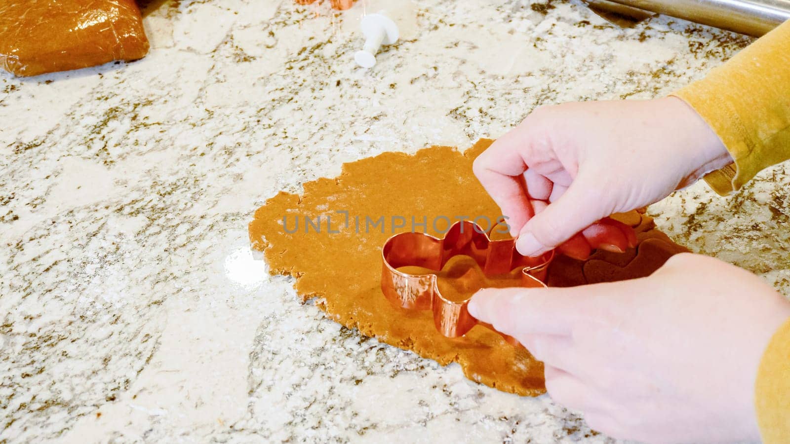 Using various festive cookie cutters, we're cutting out charming gingerbread cookies from the rolled dough on the sleek marble counter, bringing holiday cheer to the modern kitchen.