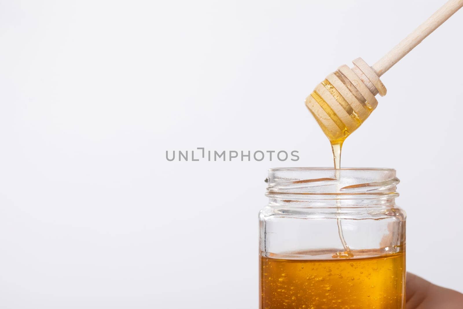 This is a closeup shot showcasing golden honey flowing gracefully from a wooden dipper into a glass jar