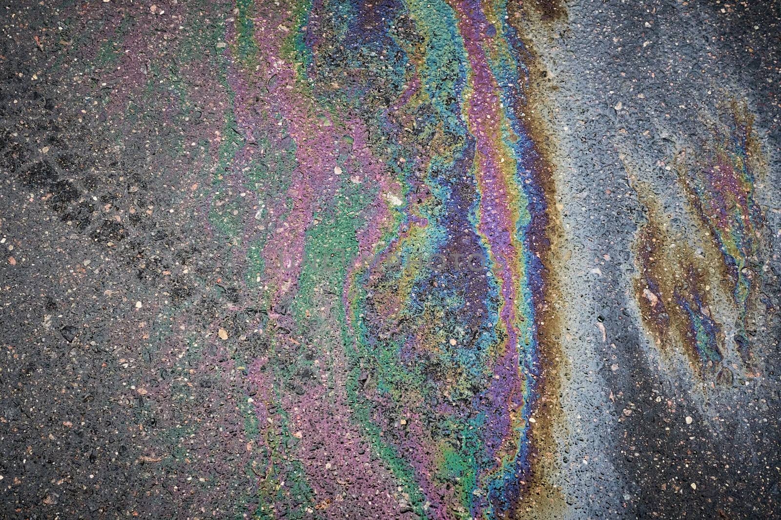 Gasoline or oil spill showing iridescent colors on asphalt road surface.