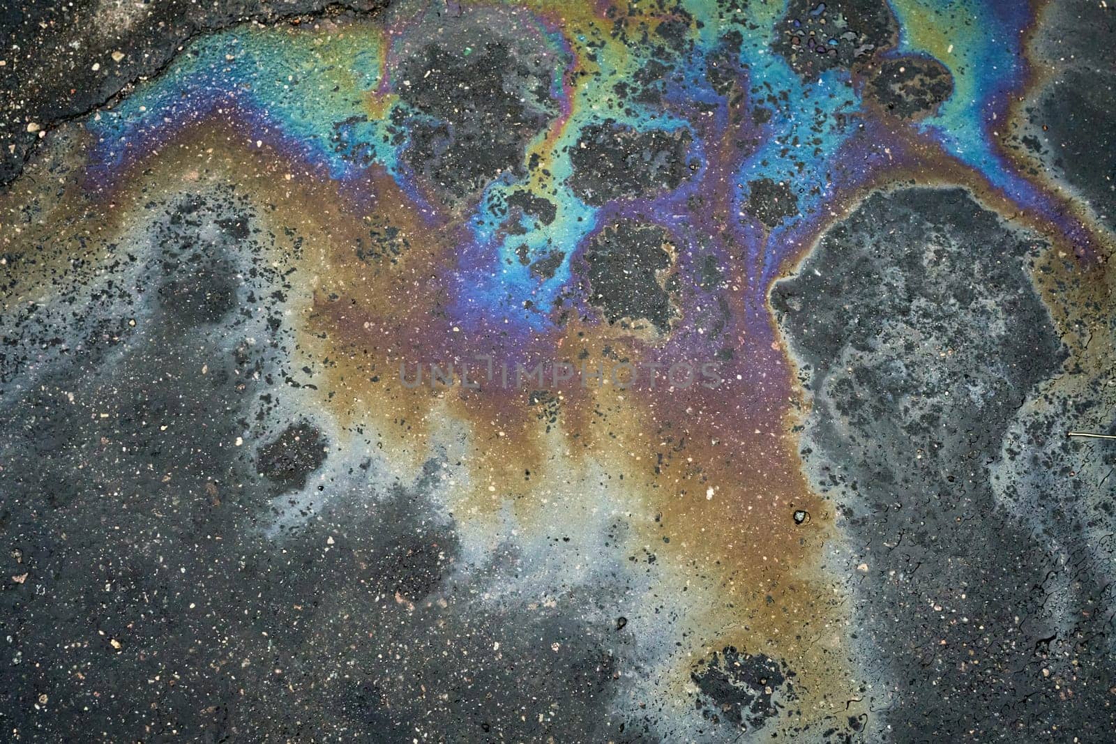 Vibrant rainbow sheen emerges on the asphalt surface as a result of an oil or gasoline spill.