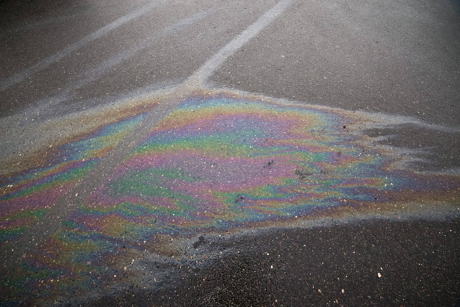 Gasoline or oil spill creating rainbow sheen on damaged asphalt parking lot.