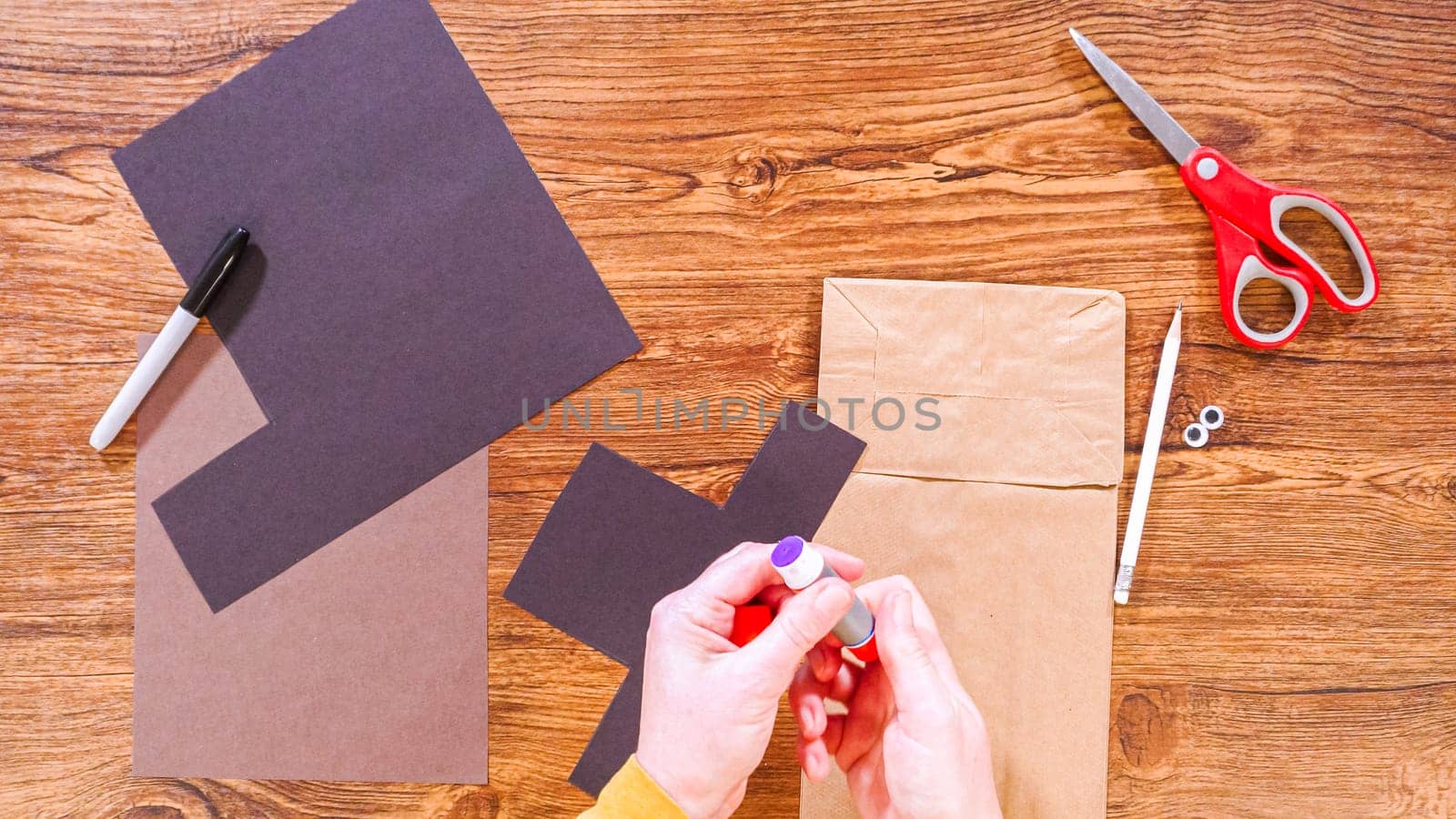 Step by step. Flat lay. Teacher guides online class through making a paper puppet from a brown bag, creatively using a wooden surface as a workspace.