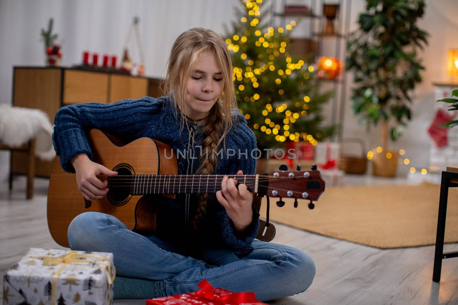 A joyful girl plays guitar among festive decorations and gifts, capturing the spirit of the holidays.