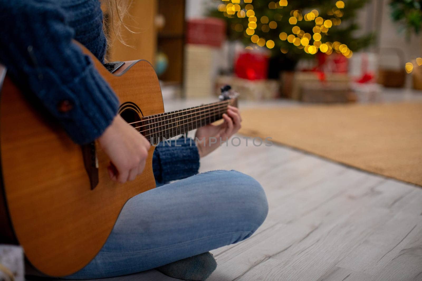A person joyfully plays an acoustic guitar in a warm, festive setting adorned with beautiful holiday lights