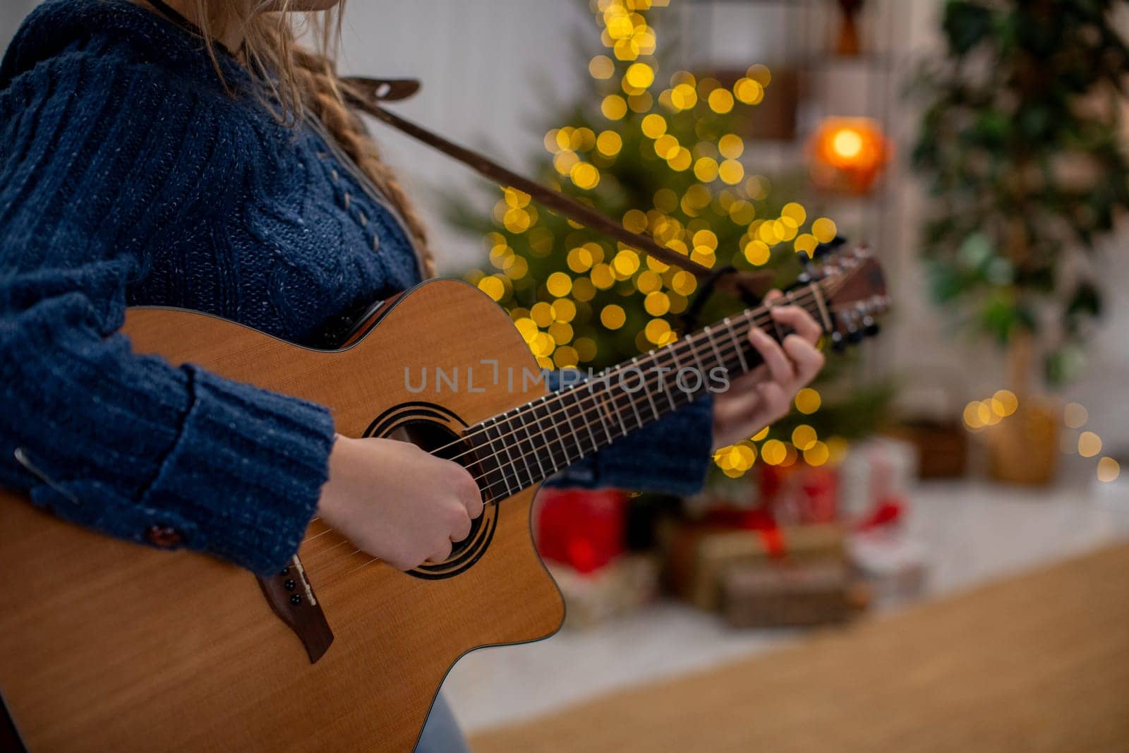 An individual strumming a guitar in close proximity to a beautifully and festively decorated Christmas tree