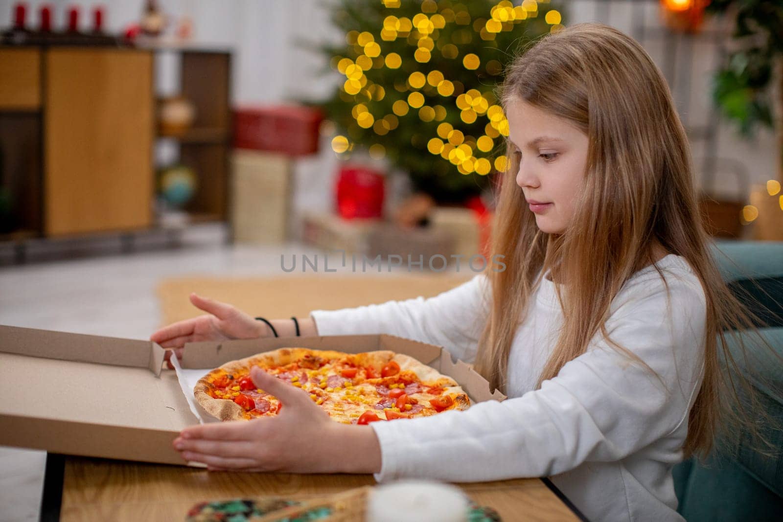 A young girl filled with joy eagerly opens a delicious pizza box in a cozy room decorated for the holiday season