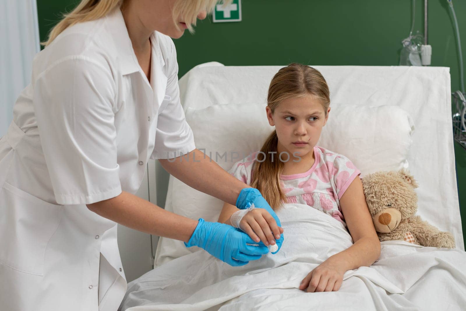 A young girl in a hospital bed receiving care from a nurse. Comforting atmosphere with a teddy bear.