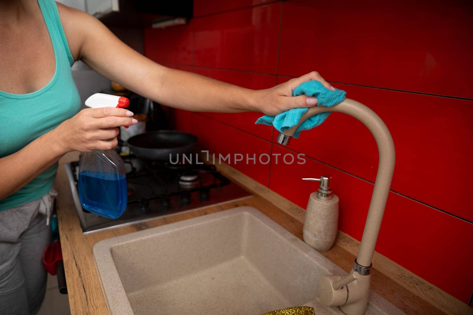 A person is diligently cleaning a kitchen faucet using a spray cleaner and a cloth in a modern, stylish kitchen