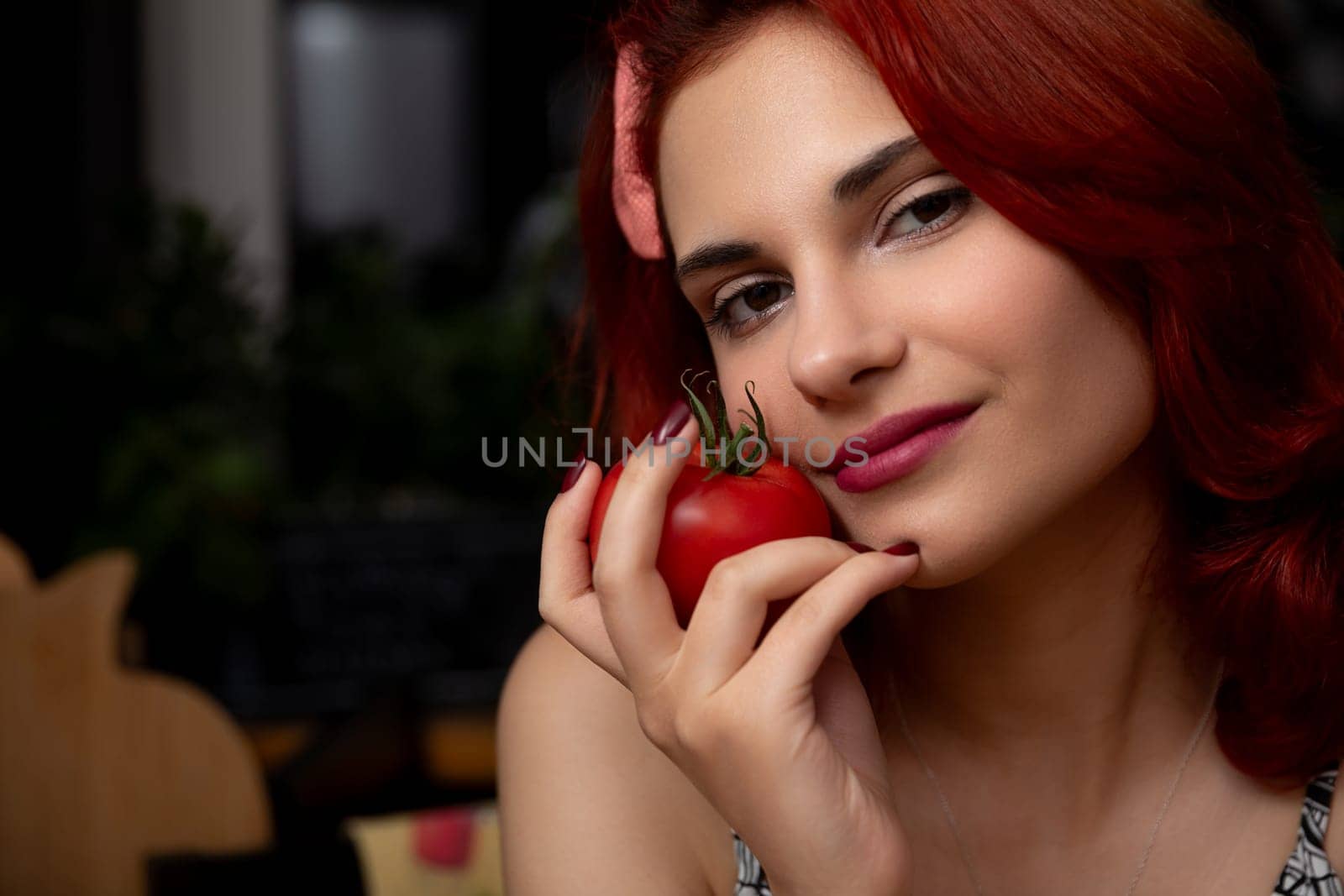 A lively young woman with striking red hair playfully holds a fresh tomato, exuding joy and creativity