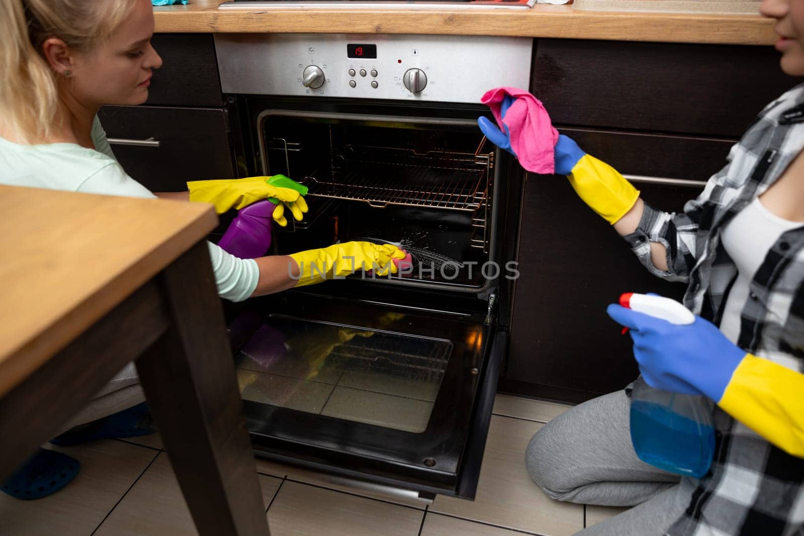 Two women in gloves are cleaning an oven, highlighting teamwork and the importance of kitchen cleanliness