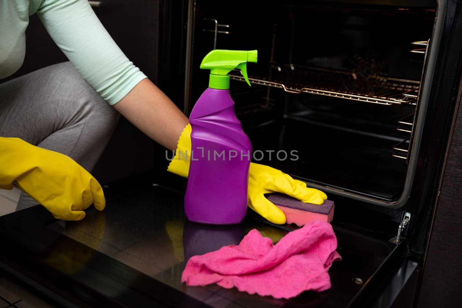 A person cleaning an oven with a colorful spray bottle and cloth, showcasing effective kitchen maintenance.