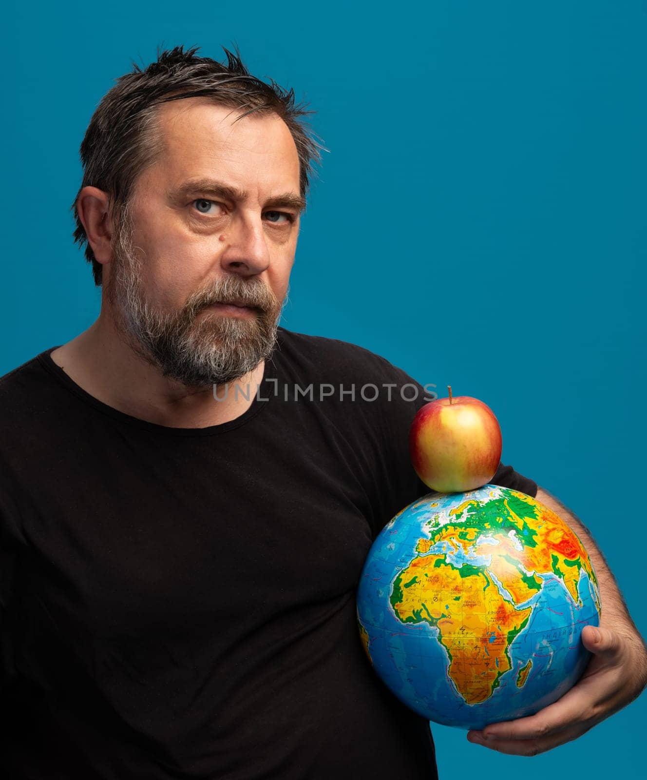 A man with a beard holds a colorful globe of the Earth in one arm and a bright red apple in the other. His serious expression highlights the connection between nature and the planets health.