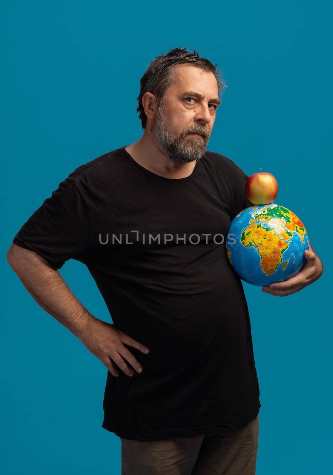 A thoughtful man stands confidently with a colorful globe in one hand and a bright red apple balanced atop it.