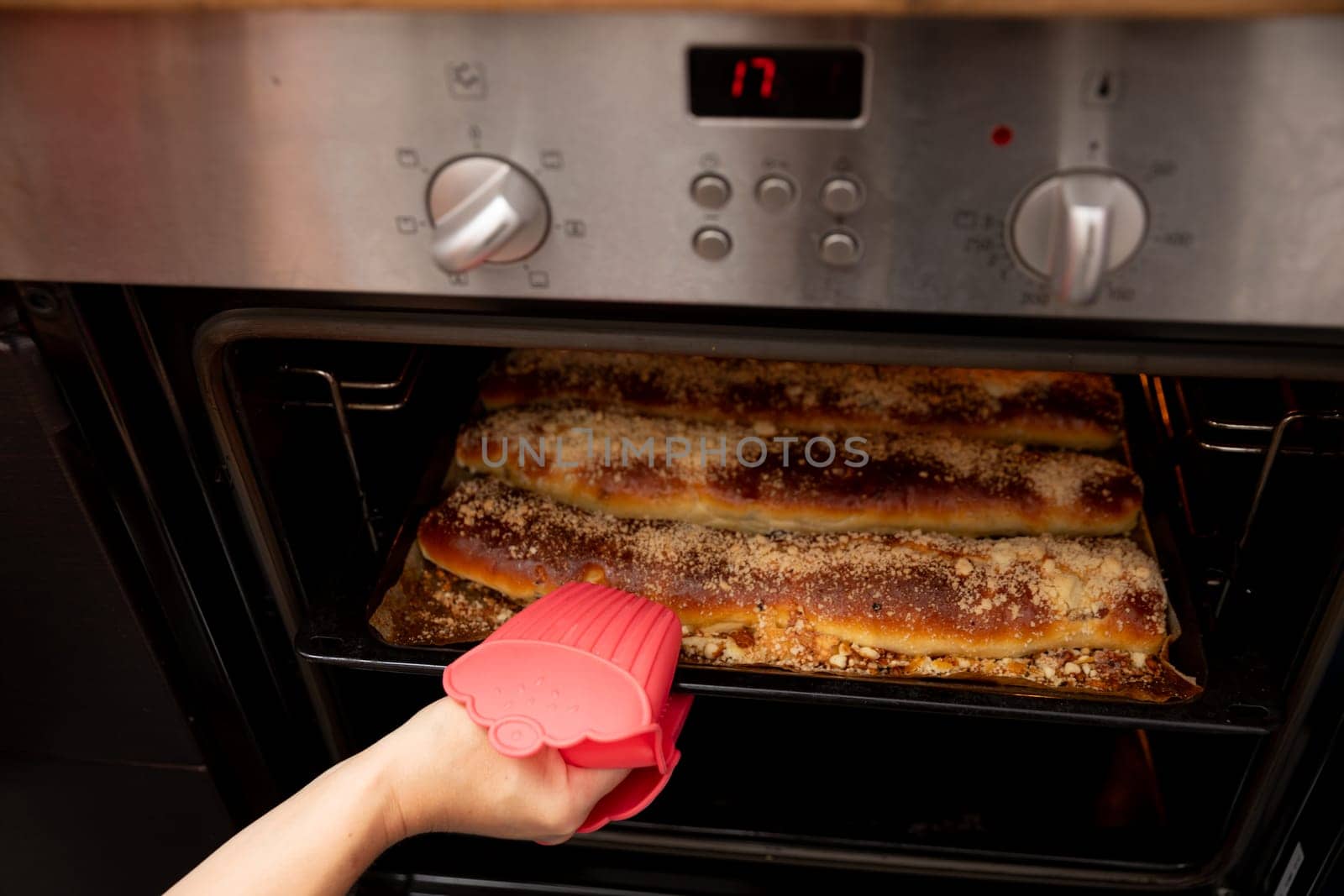 A hand wearing a silicone mitt is carefully reaching into a hot oven to retrieve some freshly baked goods