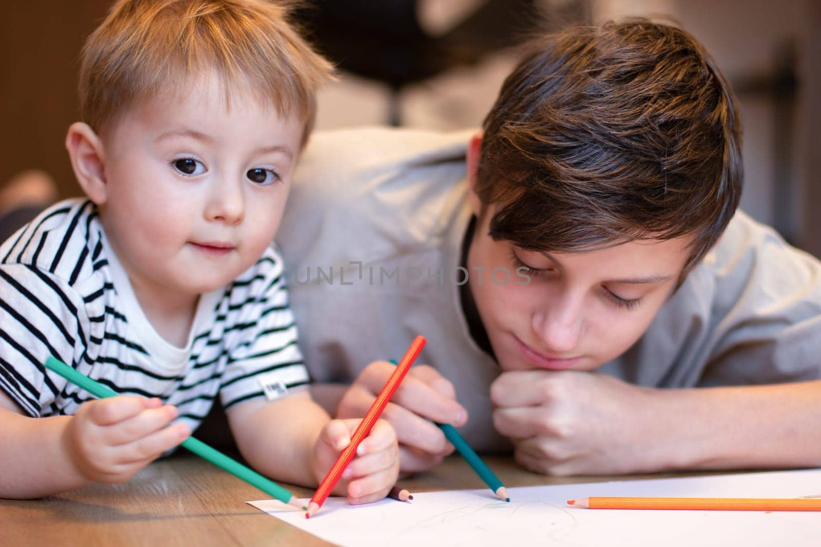 Two children draw with colored pencils. A teenager and a younger brother draw while lying on the floor. High quality photo