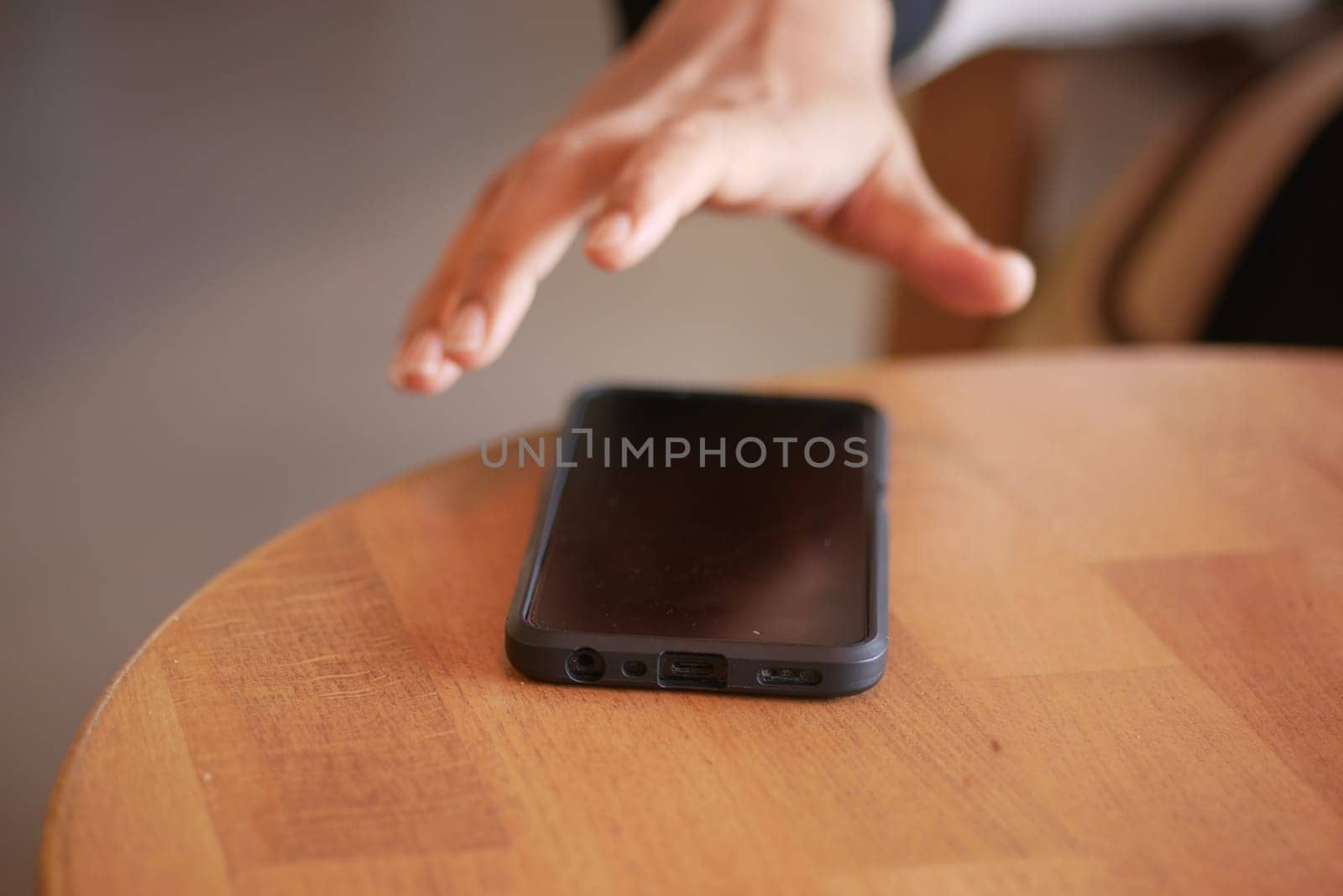 A hand grabbing and picking up mobile phone on the table