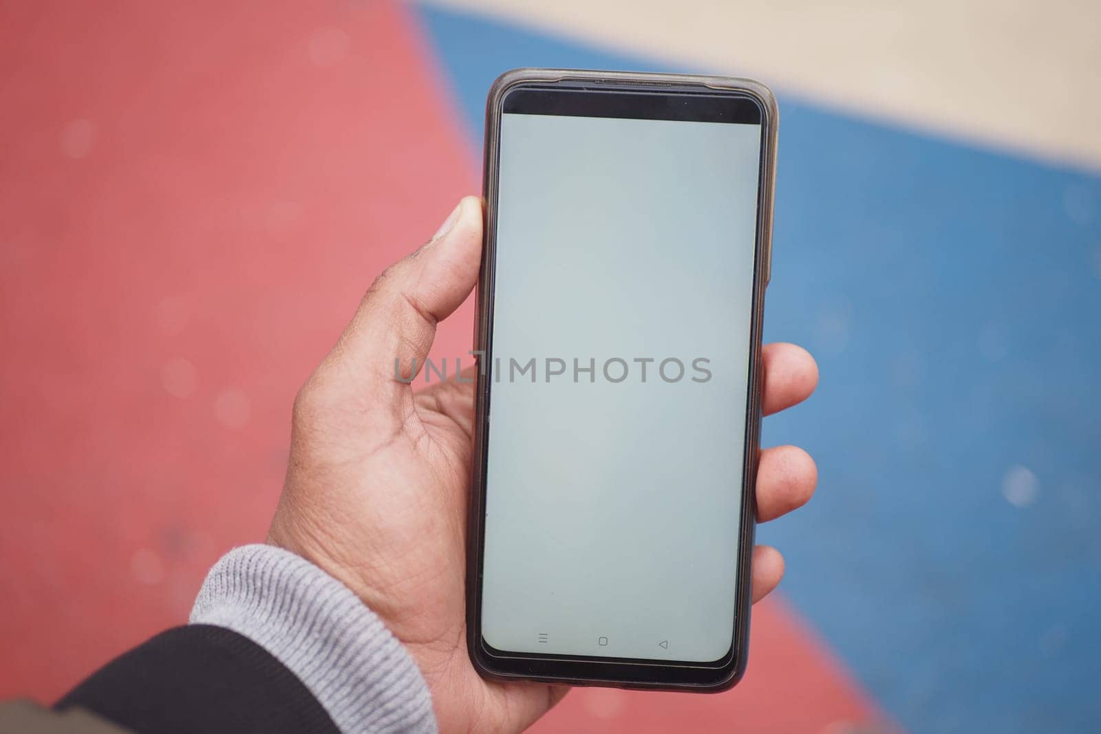 A hand showcasing a smartphone with a blank screen against a vibrant background.