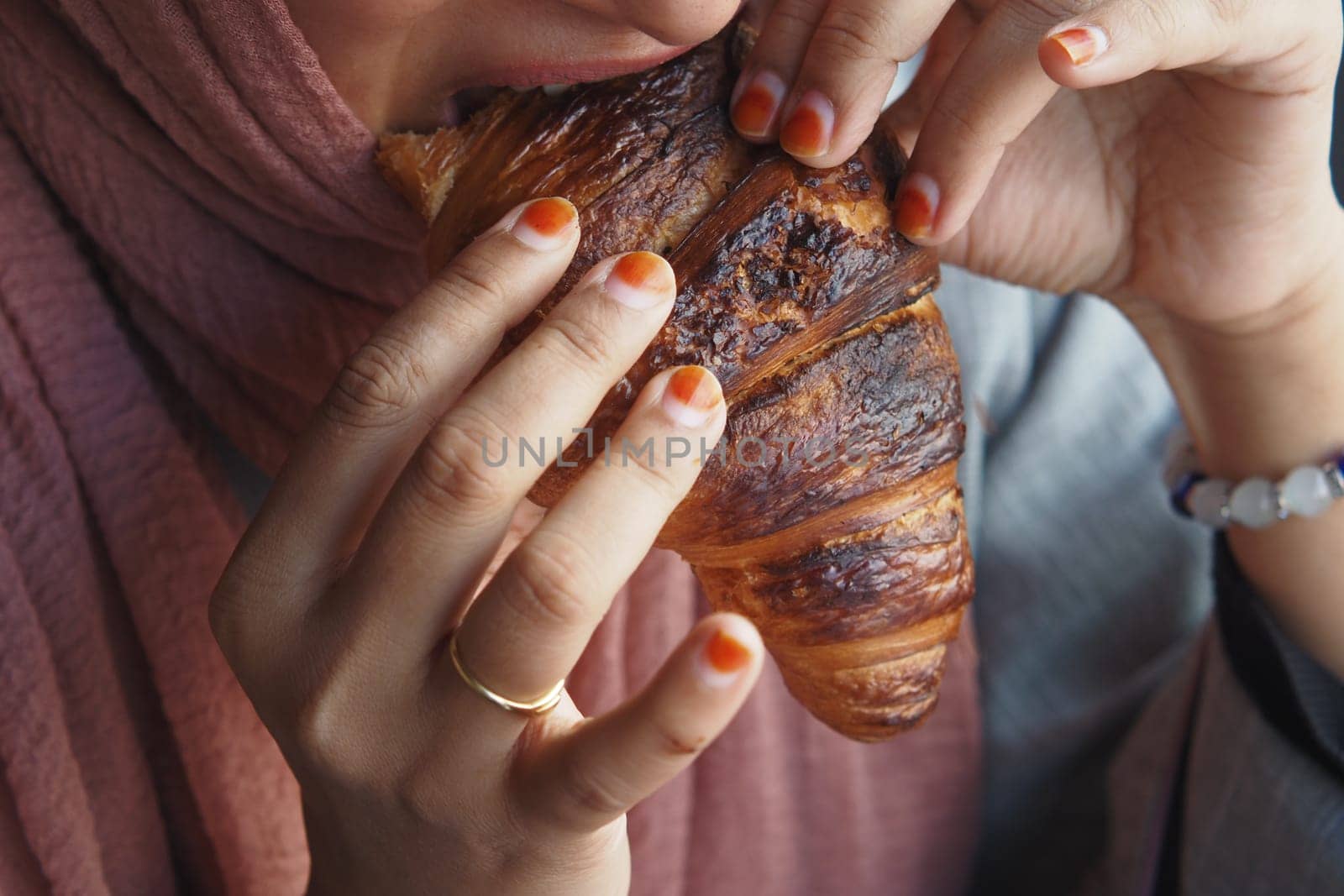 A woman is savoring a warm and delicious croissant while sitting in a cozy and inviting setting