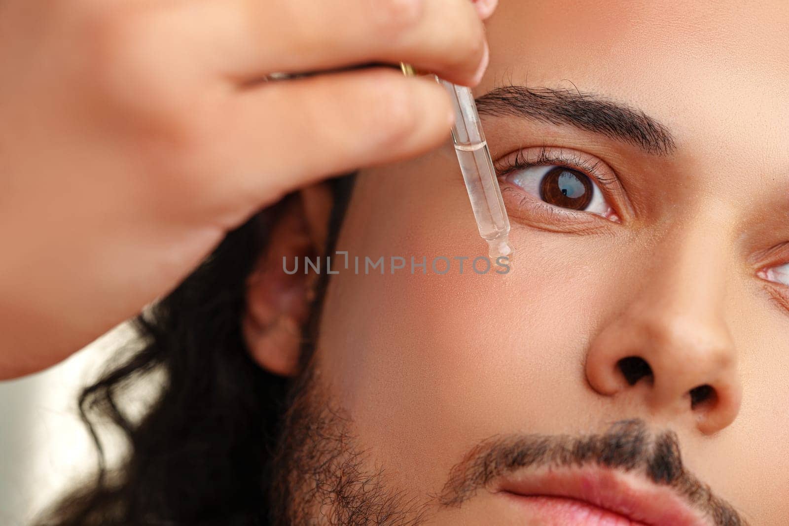 A close-up of a man applying a serum drop to his face, showcasing skincare routine