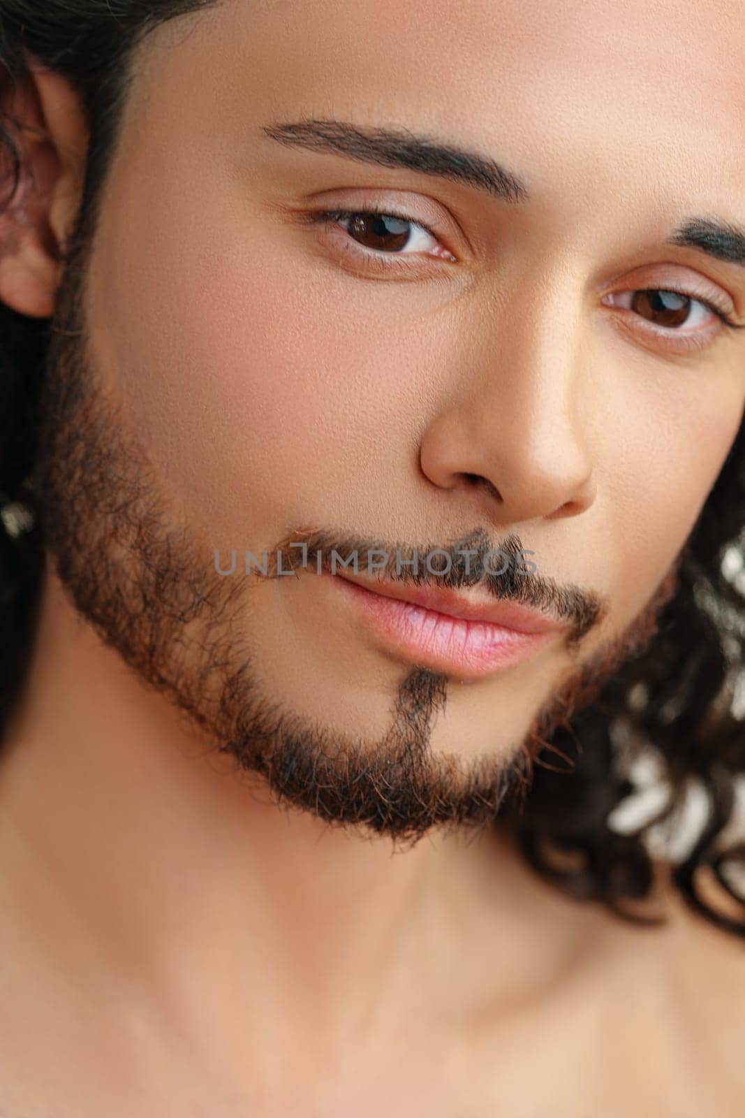 Close-up portrait of a man with long curly hair and a well-groomed beard showcasing clear skin