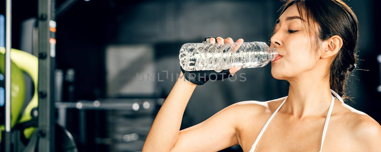 Asian woman guy hydrated by drinking water sports from a bottle in gym after cardio work out, female tired with liquid bottle drink after training at fitness gym, workout healthy lifestyle concept