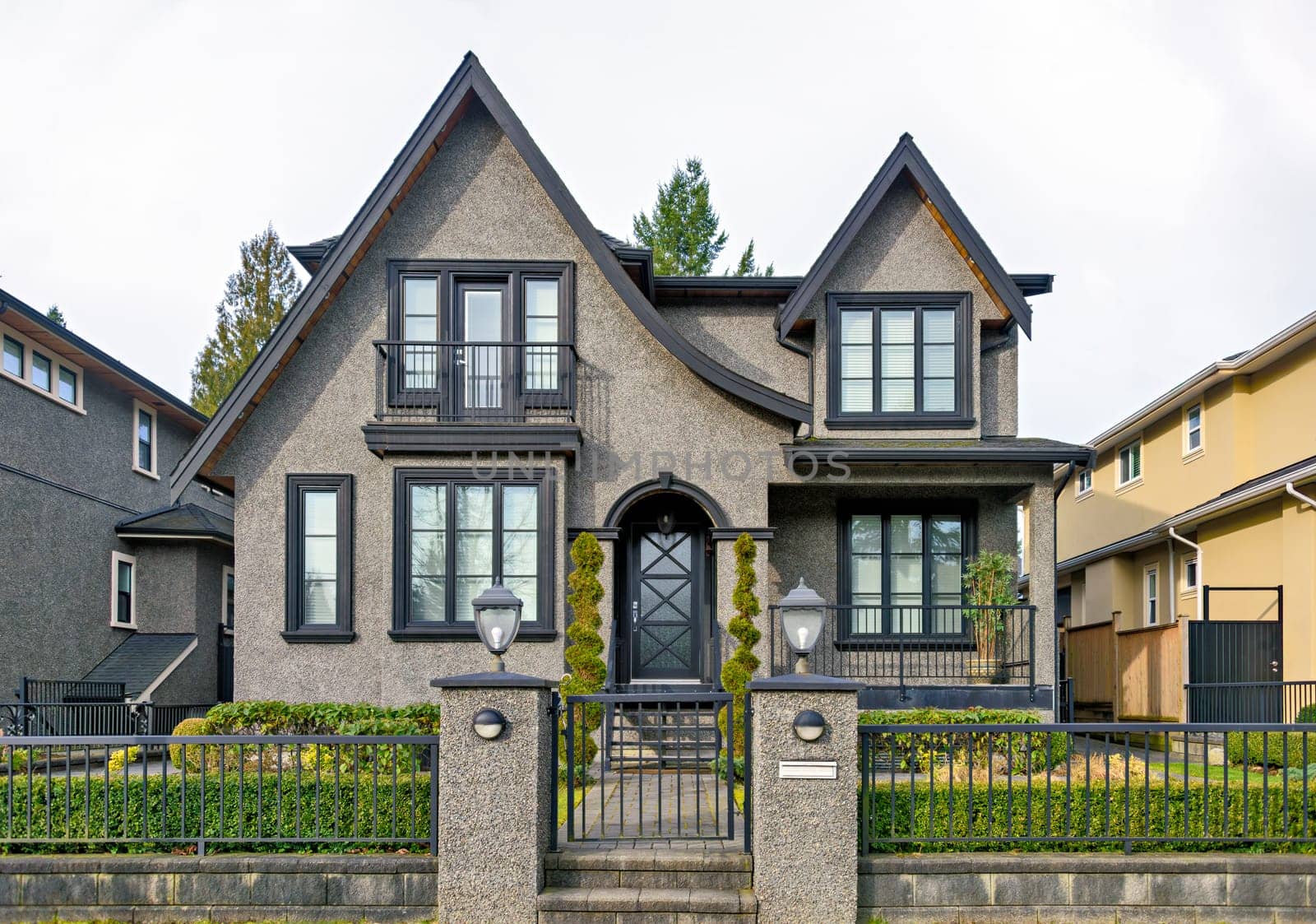 Gloomy residential house with metal fence in front on overcast sky background.
