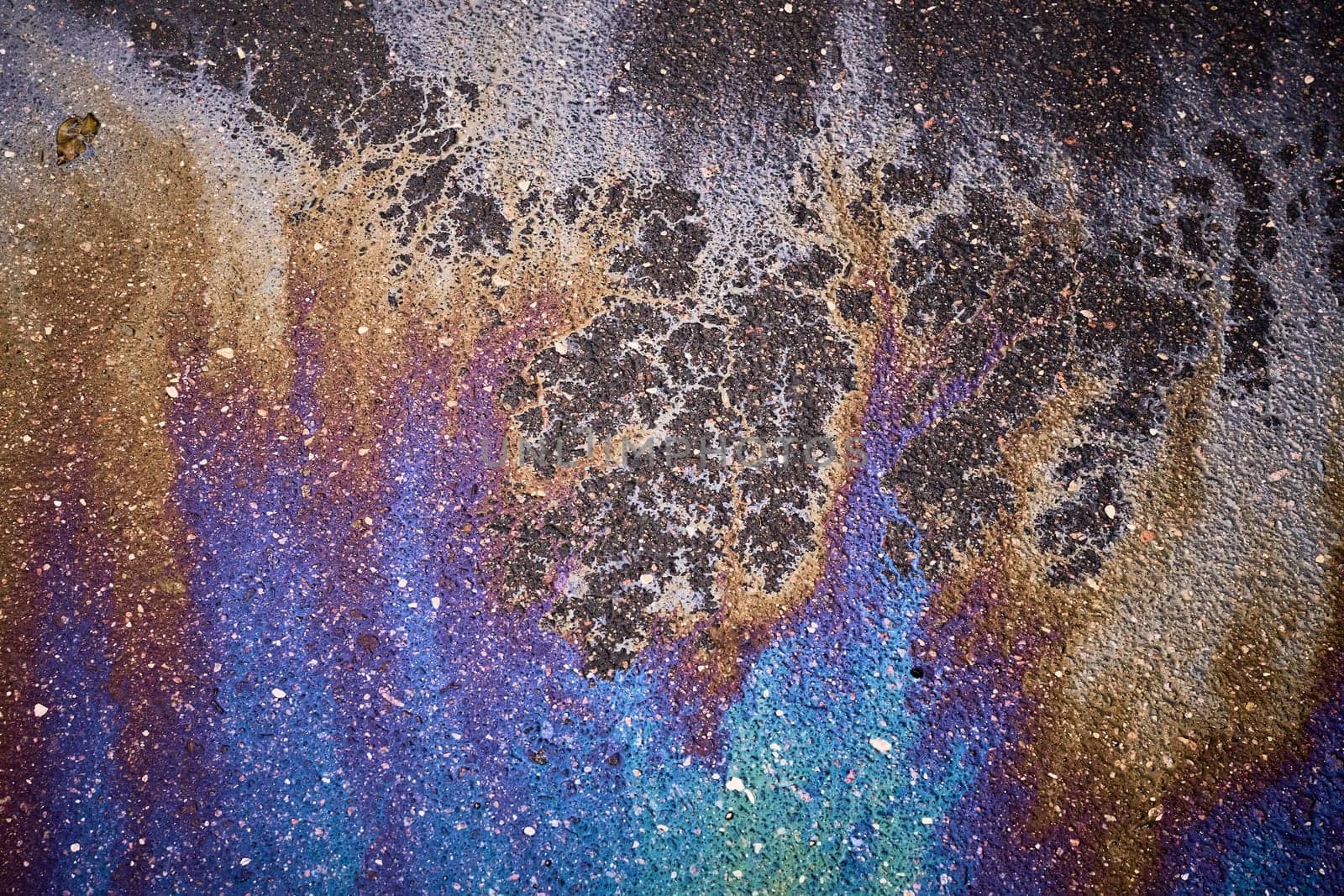 Colorful gasoline or oil spill creating a rainbow chemical reaction on asphalt road surface.