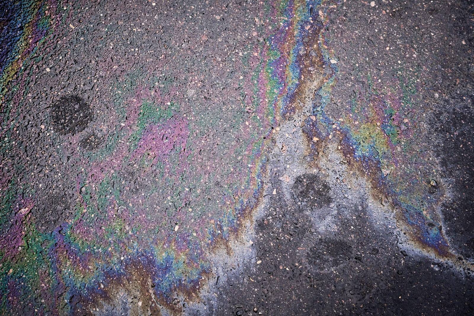 Colorful gasoline or oil spill creating a rainbow pattern on asphalt, indicating pollution and environmental damage.