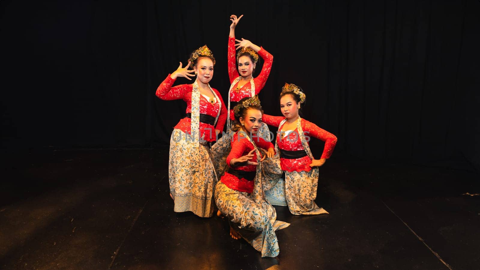 A group of traditional Sundanese dancers radiate elegant charm to the audience with their movements and red costumes on stage at night