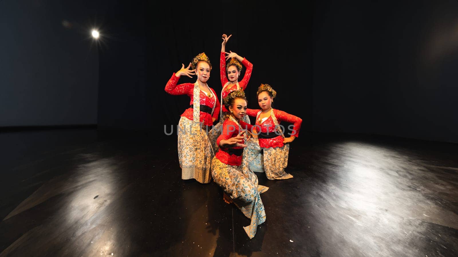 A group of traditional Sundanese dancers radiate elegant charm to the audience with their movements and red costumes on stage at night