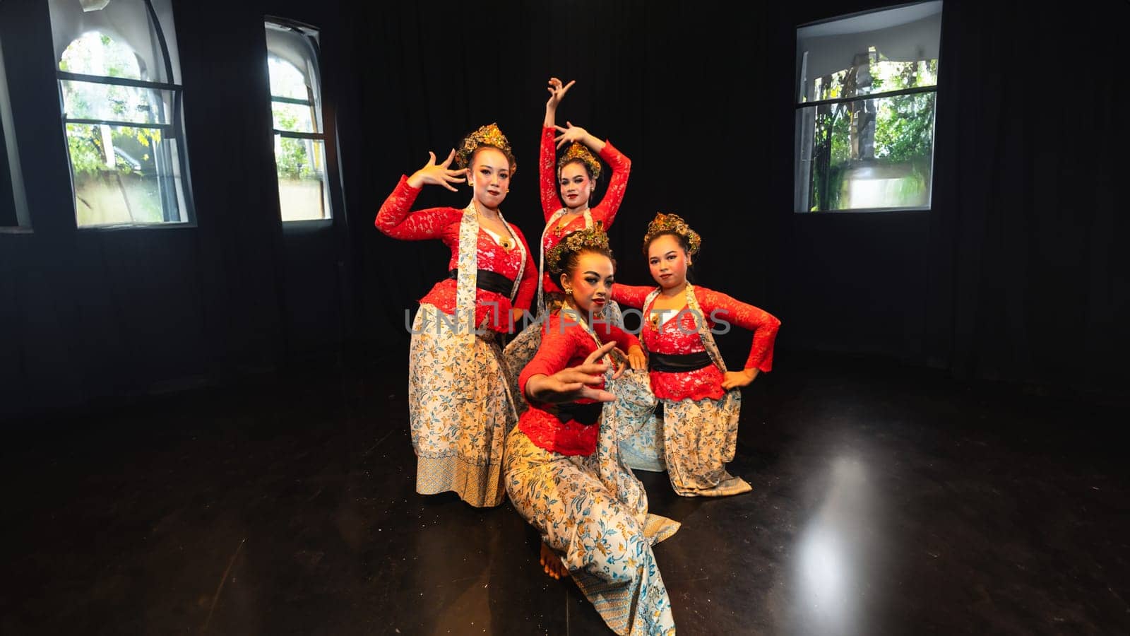 A group of traditional Sundanese dancers radiate elegant charm to the audience with their movements and red costumes on stage at night