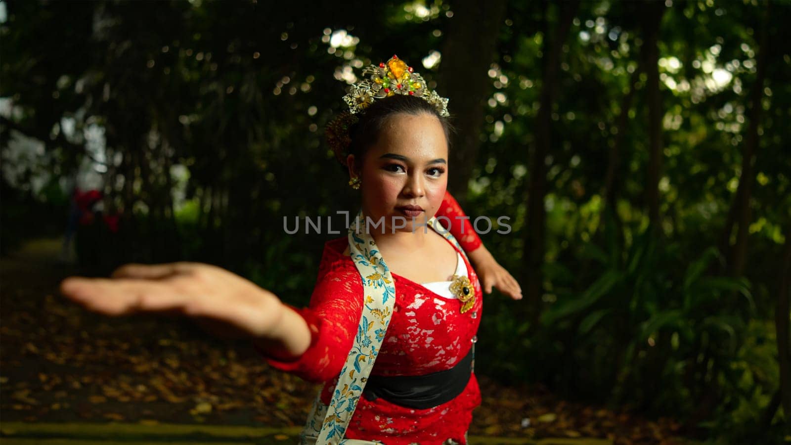 A traditional Indonesian dancer wearing a red costume decorated with sequins and embroidery looks luxurious in the dancer's performance in the forest in the morning