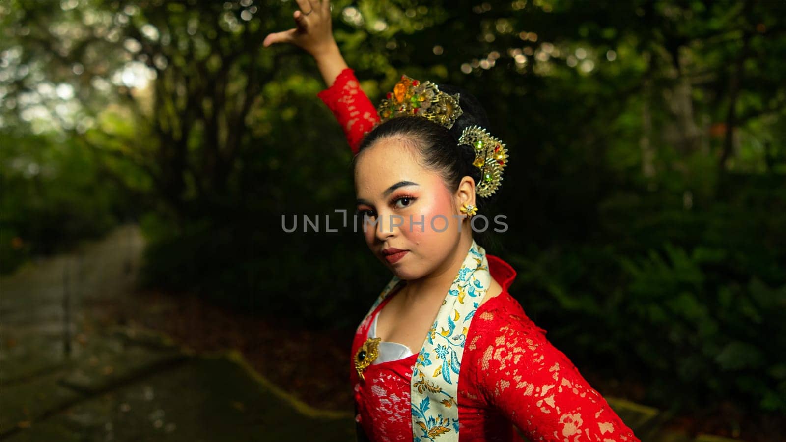 A traditional Indonesian dancer wearing a red costume decorated with sequins and embroidery looks luxurious in the dancer's performance in the forest in the morning