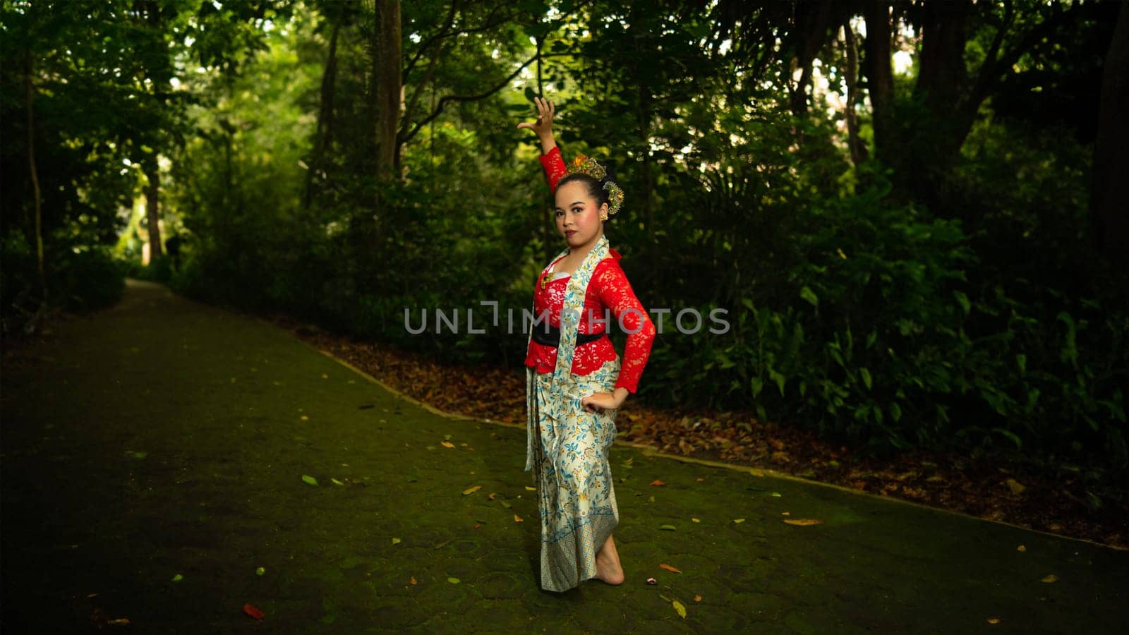 A traditional Indonesian dancer wearing a red costume decorated with sequins and embroidery looks luxurious in the dancer's performance in the forest in the morning
