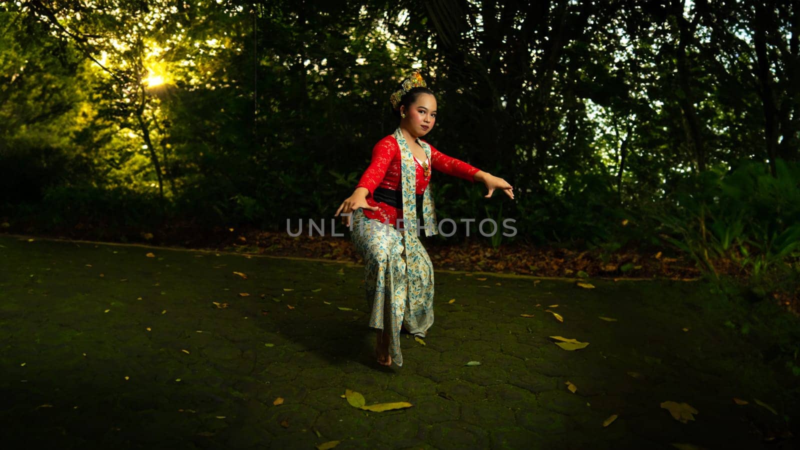 A traditional Indonesian dancer wearing a red costume decorated with sequins and embroidery looks luxurious in the dancer's performance in the forest in the morning
