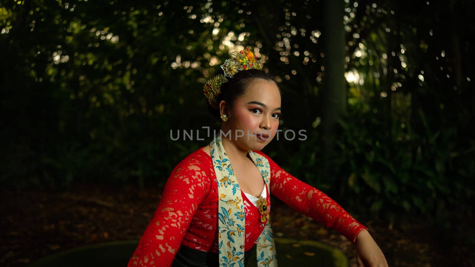 A traditional Indonesian dancer wearing a red costume decorated with sequins and embroidery looks luxurious in the dancer's performance in the forest in the morning
