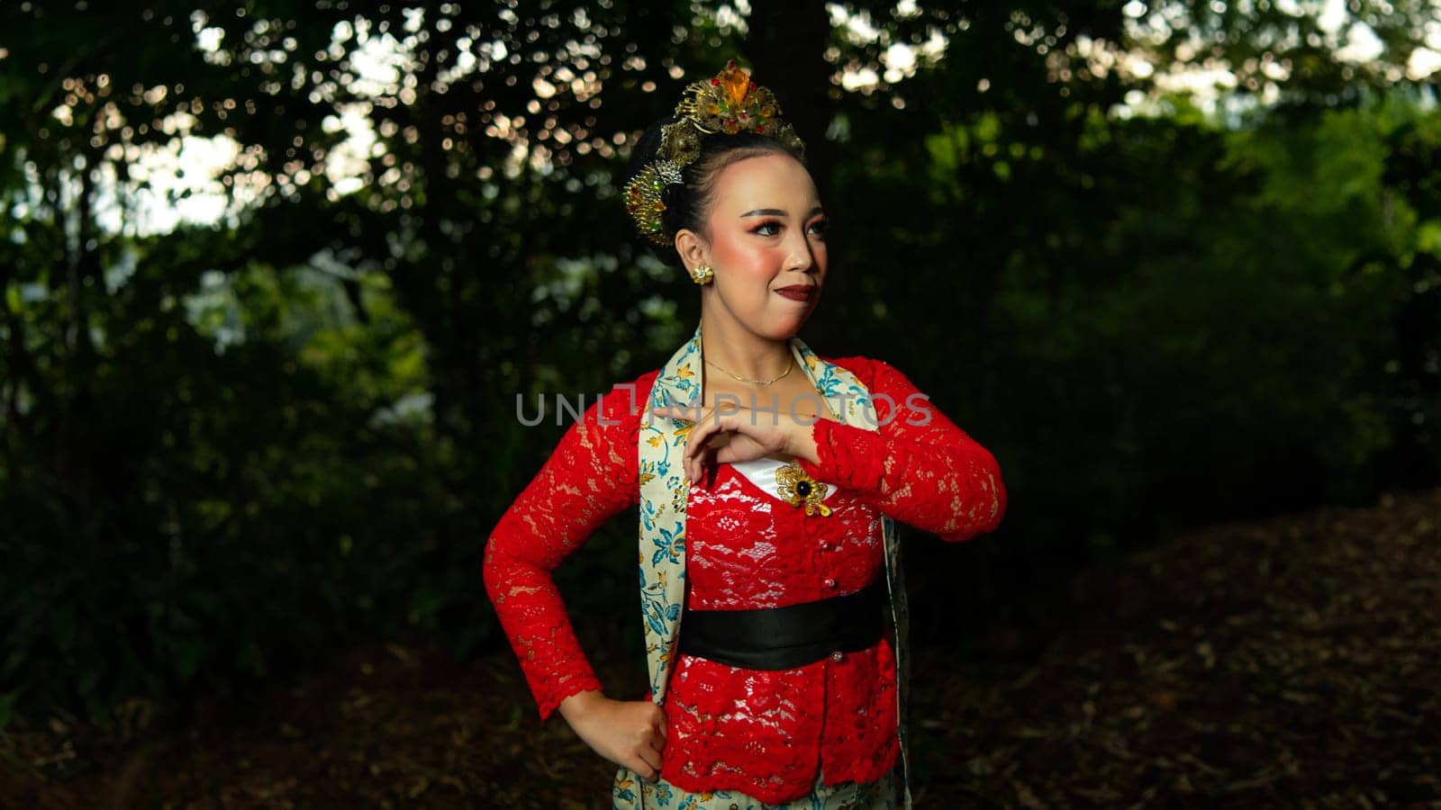 a traditional Balinese dancer wearing a red costume which is a symbol of cultural preservation with beautiful motifs while in the forest in the morning