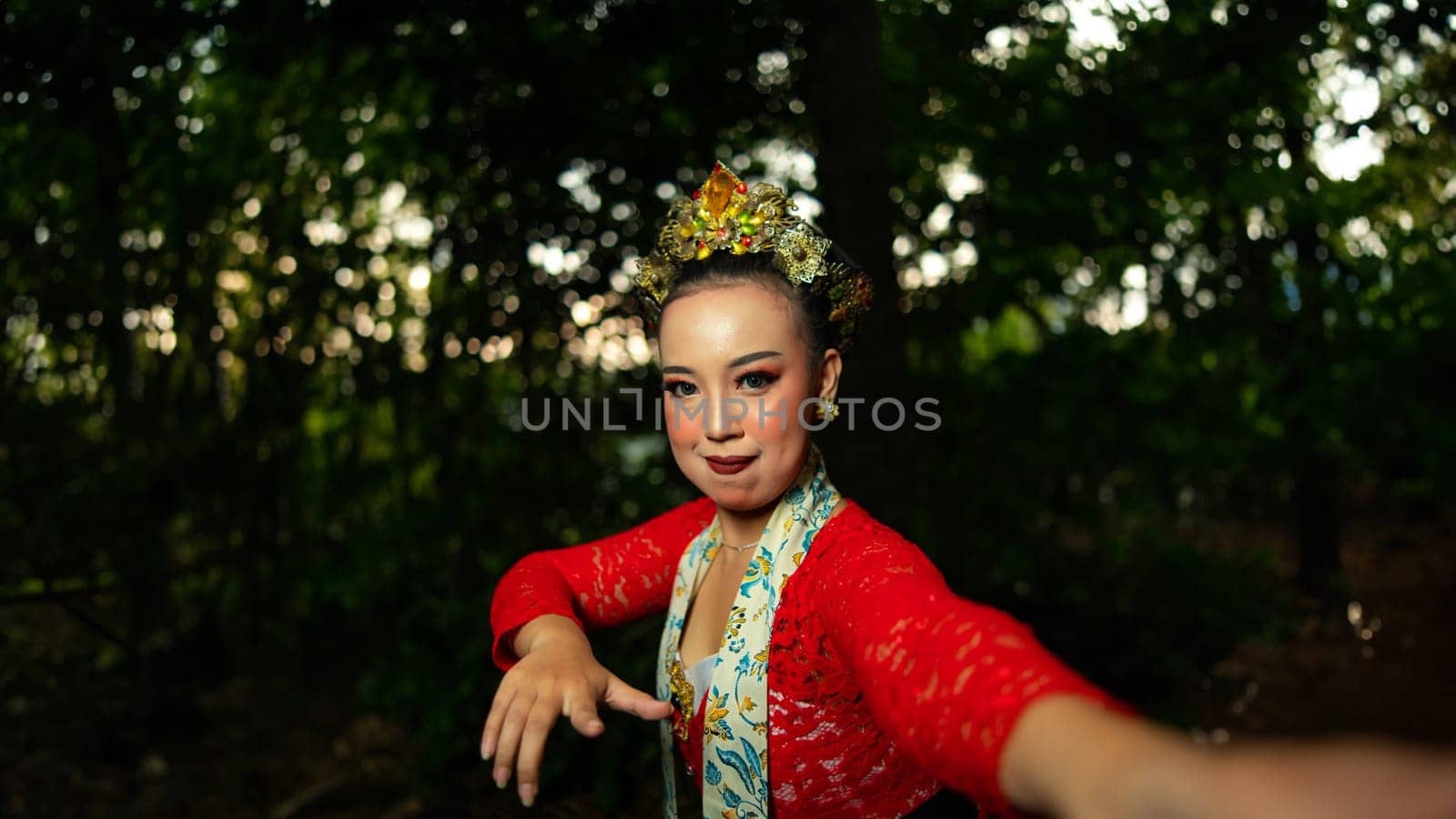 a traditional Balinese dancer wearing a red costume which is a symbol of cultural preservation with beautiful motifs while in the forest in the morning