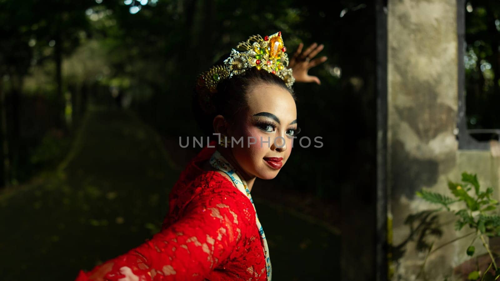 A traditional Indonesian dancer dazzles with her beautiful appearance while wearing a red costume that catches the eye of the audience in the forest in the morning