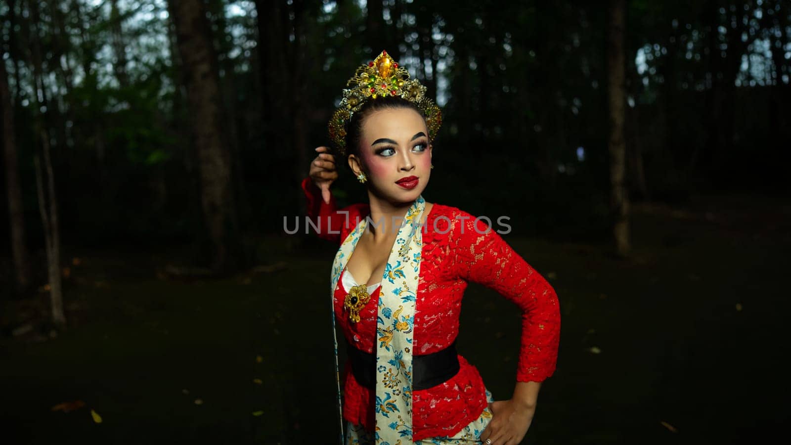 A traditional Indonesian dancer dazzles with her beautiful appearance while wearing a red costume that catches the eye of the audience in the forest in the morning