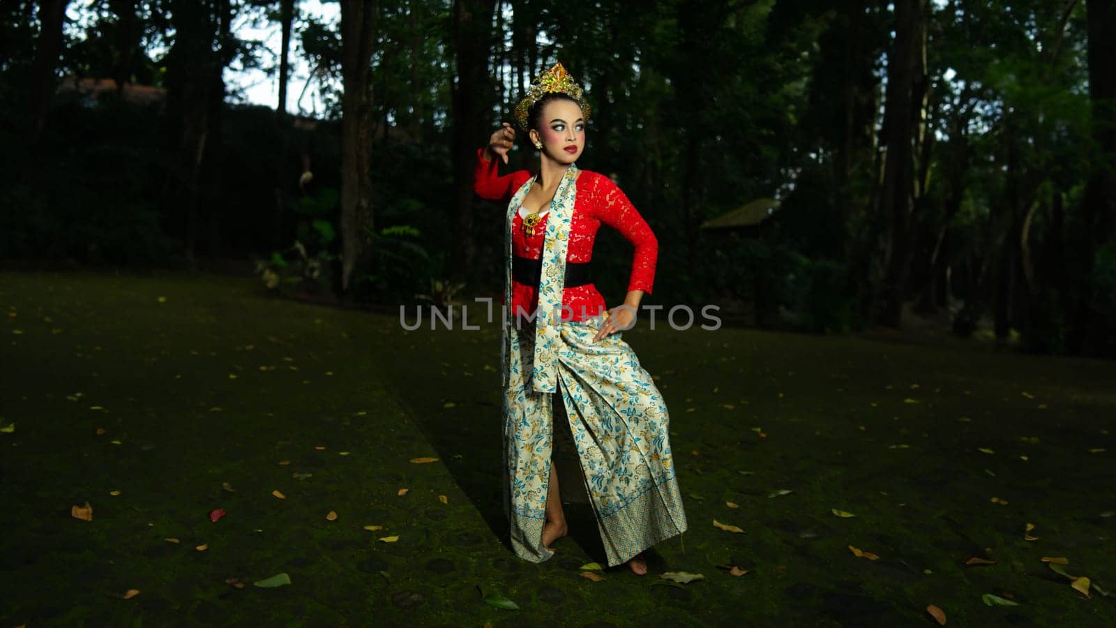 A traditional Indonesian dancer dazzles with her beautiful appearance while wearing a red costume that catches the eye of the audience in the forest in the morning