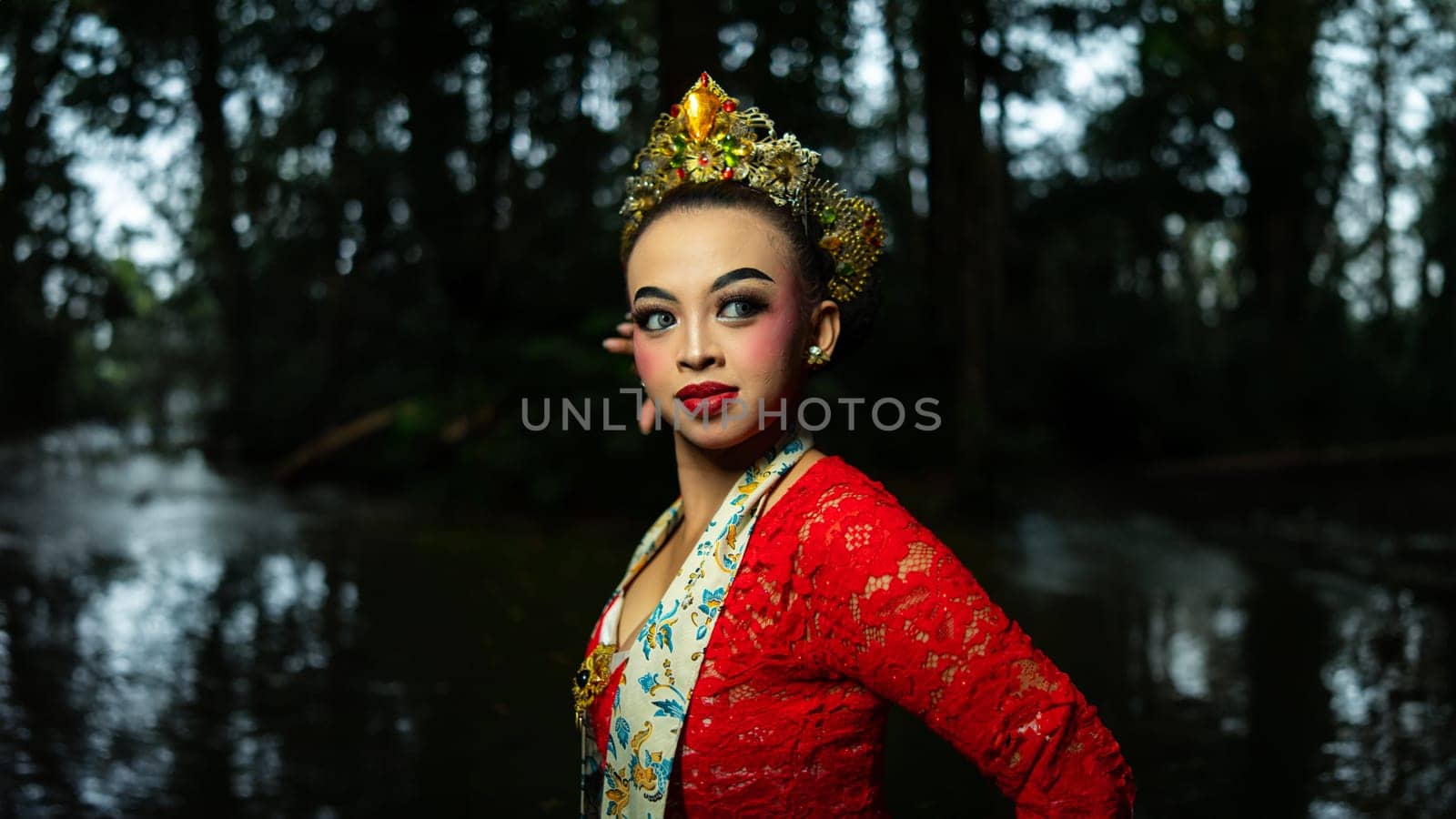 A traditional Indonesian dancer dazzles with her beautiful appearance while wearing a red costume that catches the eye of the audience in the forest in the morning