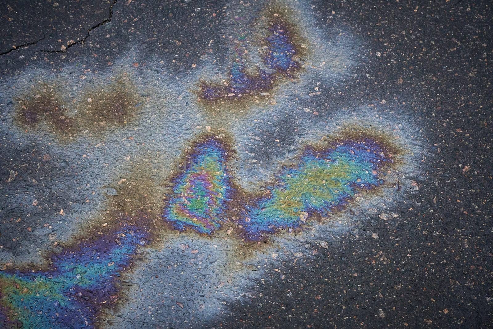 Colorful gasoline spill creates an abstract pattern on a dark asphalt road.
