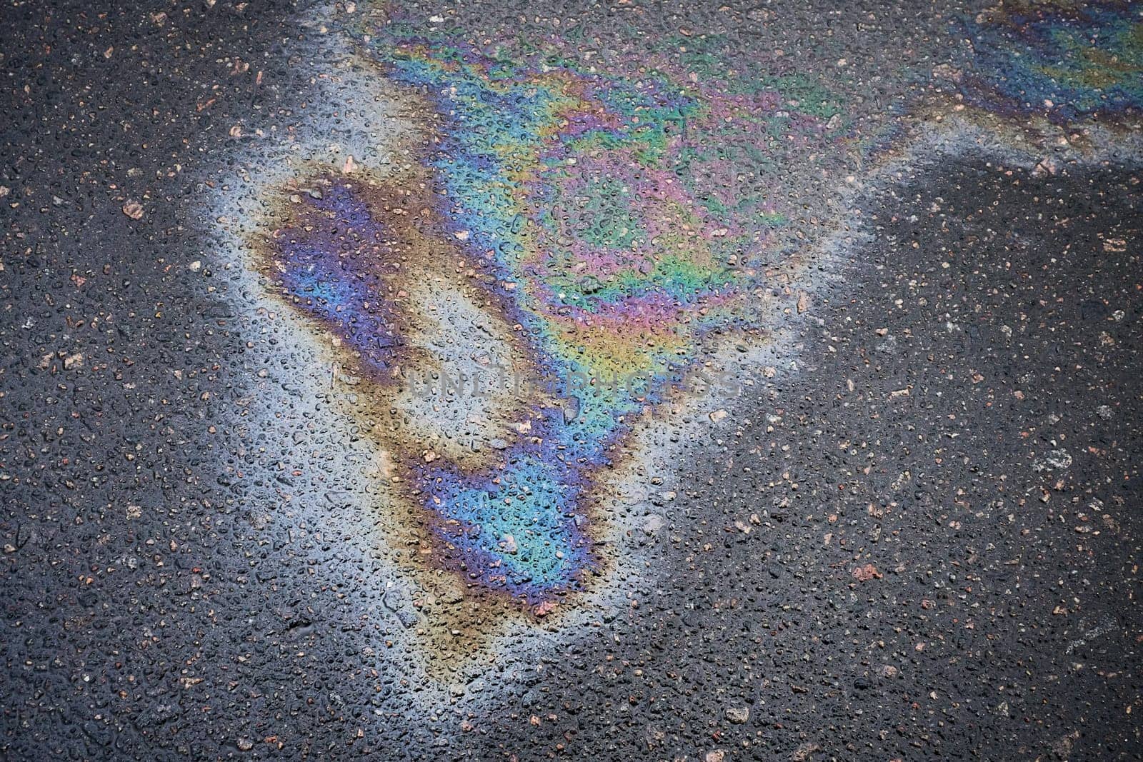 Asphalt oil stain, bright gasoline spots on the road surface as a texture or background.