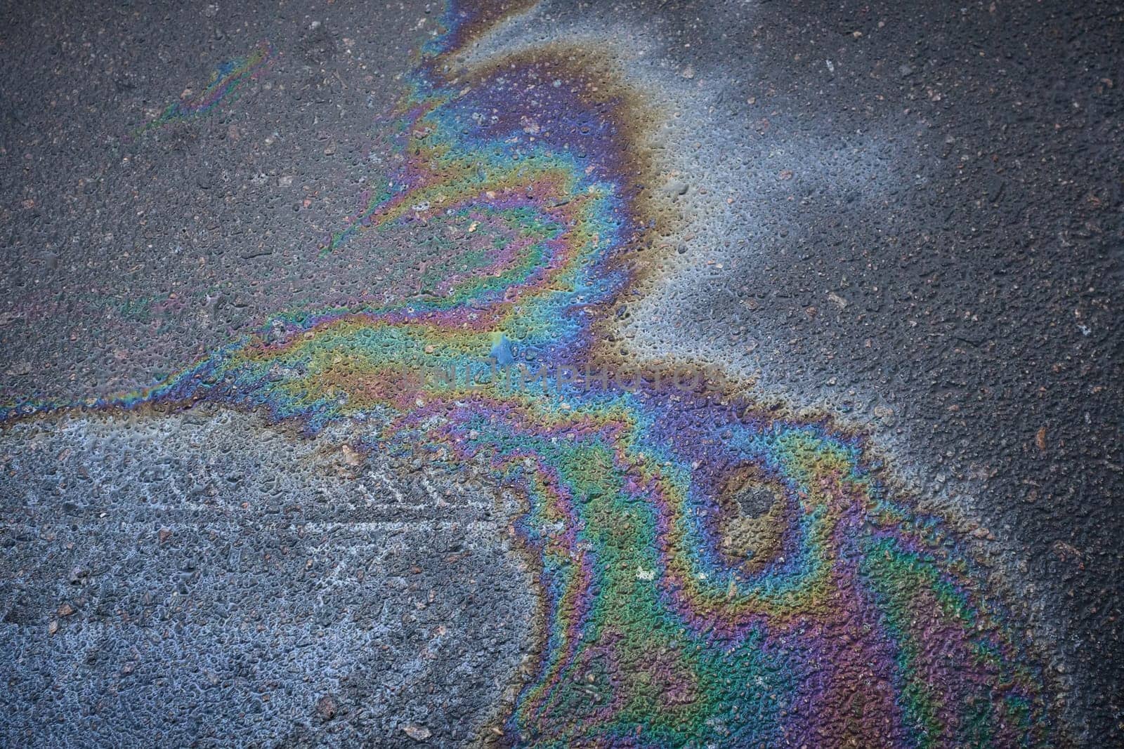 Gasoline or oil spill creating rainbow pattern on asphalt road.