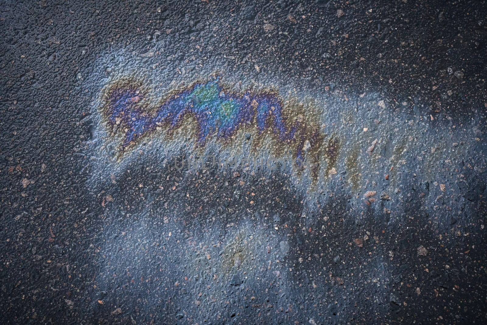 Gasoline spill showing iridescent colors on asphalt road.